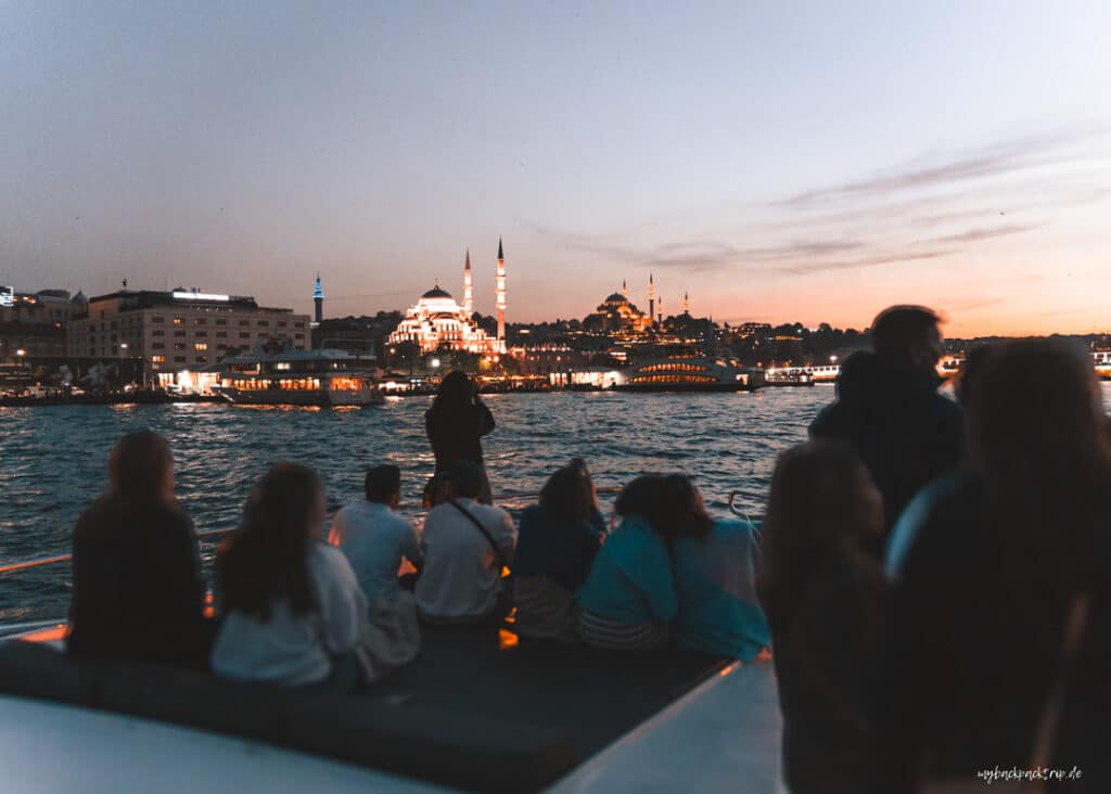 Nächtliche Bosporus-Schifffahrt in Istanbul mit erleuchteten Sehenswürdigkeiten und Passagieren auf dem Boot.